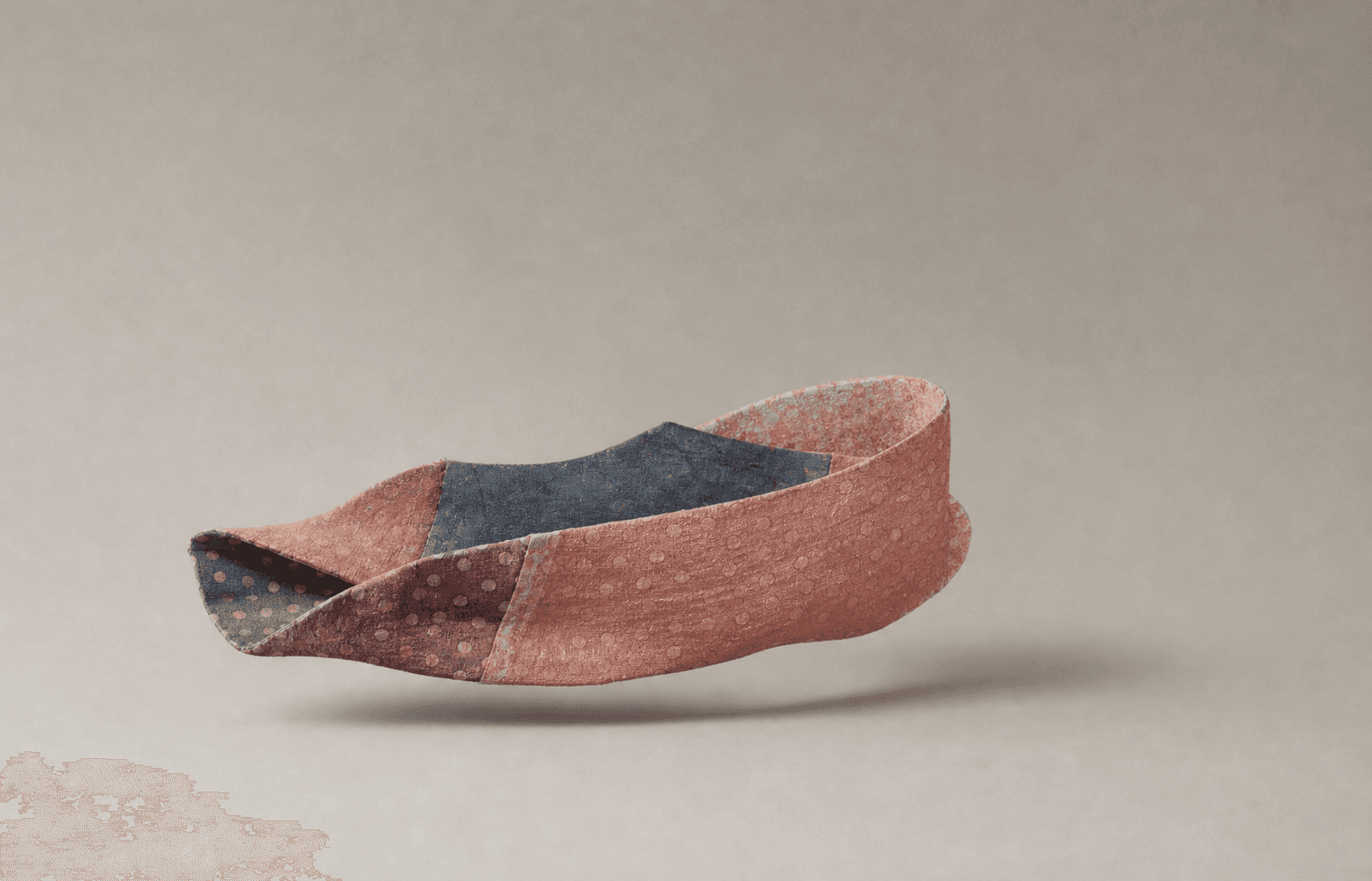 A folded textile ribbon sculpture floating against a warm neutral background.